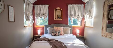 A bedroom with a bed, two bedside tables with lamps, a mirror, and curtains.