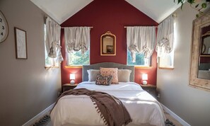 Un dormitorio con una cama, dos mesitas de noche con lámparas, un espejo y cortinas.