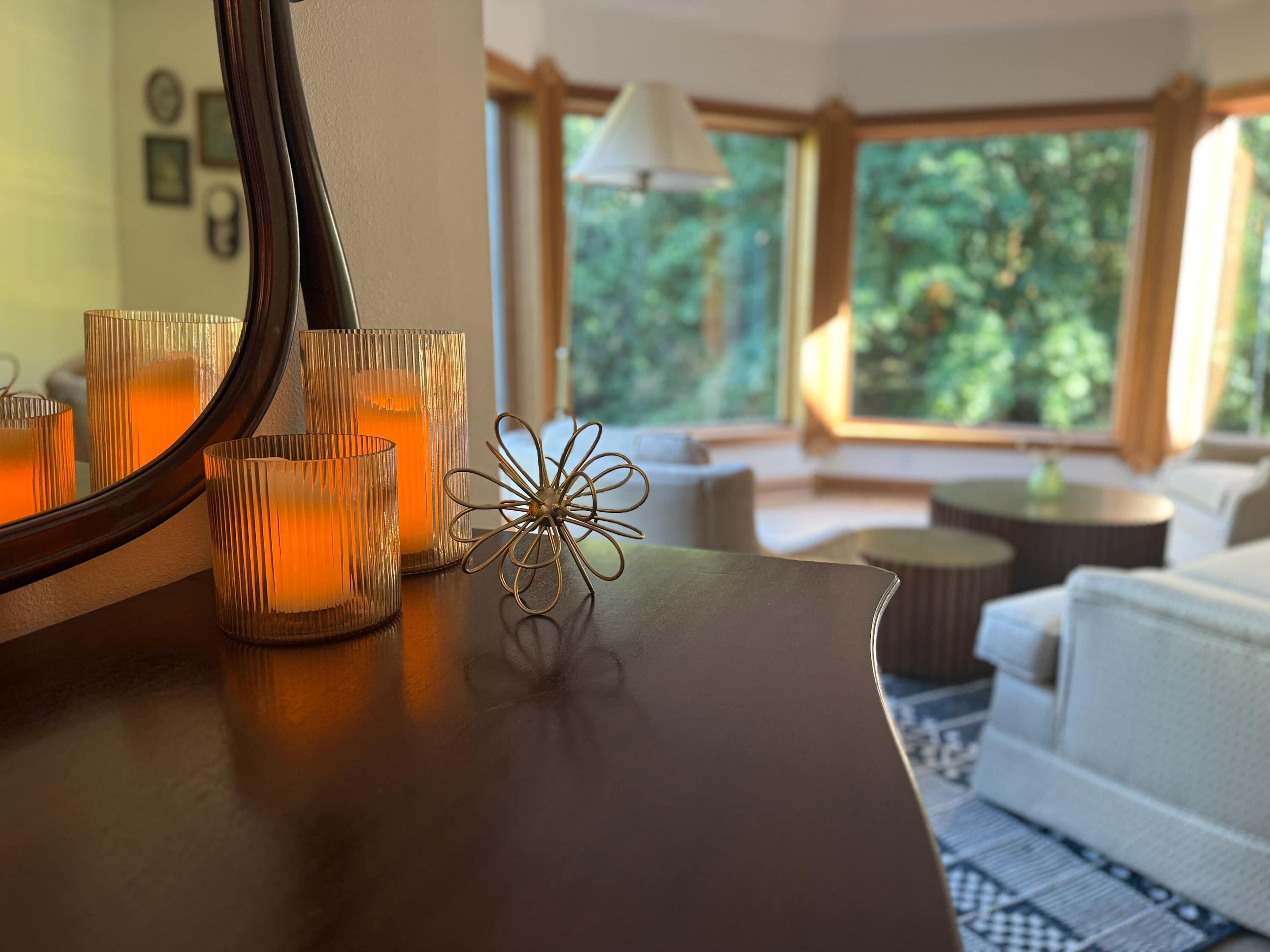 Une pièce avec une table en bois, des bougies, un objet décoratif en métal et une vue sur la verdure grâce à de grandes fenêtres.