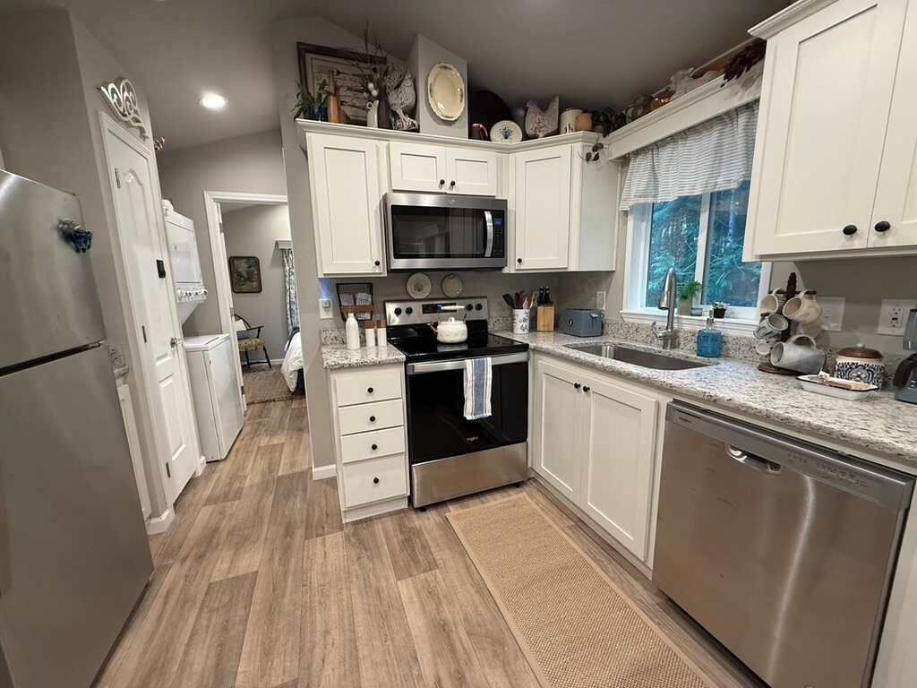 Una cocina con gabinetes blancos, electrodomésticos de acero inoxidable, microondas, horno y lavavajillas.