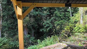 Une structure de pergola en bois, dotée d’un toit et entourée d’une végétation forestière dense.