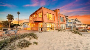 A beachfront property with a modern two-story building, a sandy beach in the foreground, and a clear sky.
