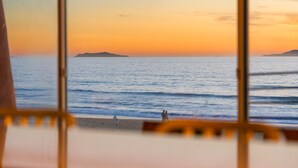 A view through a window of a beach at sunset with calm waters and distant landforms.