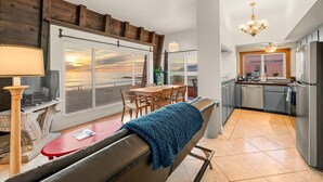 A modern kitchen with a view of the beach, a dining area with a bench, and a chandelier.
