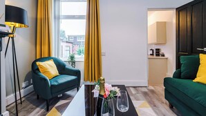 Una sala de estar moderna con un sofá verde, un sillón a juego y una mesa de centro con una botella y un vaso.