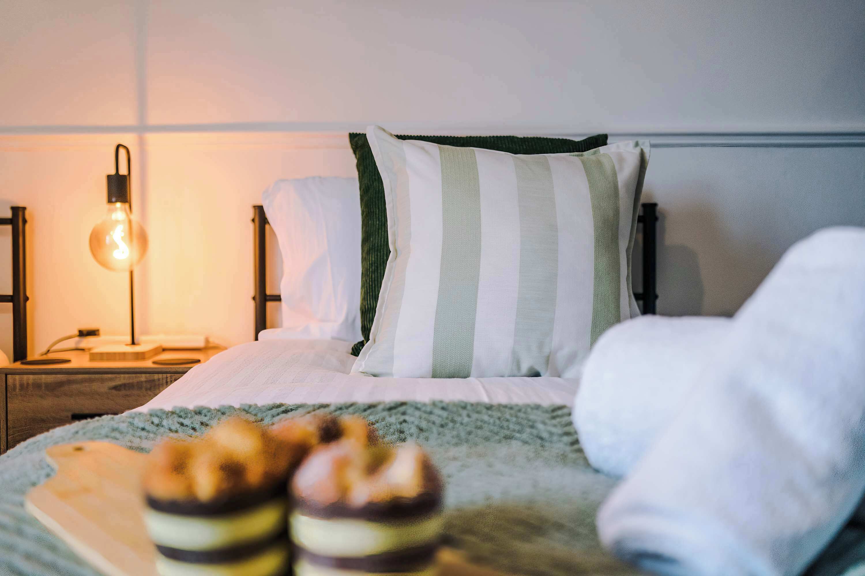 Una cama bien hecha con almohadas a rayas y una lámpara de noche.