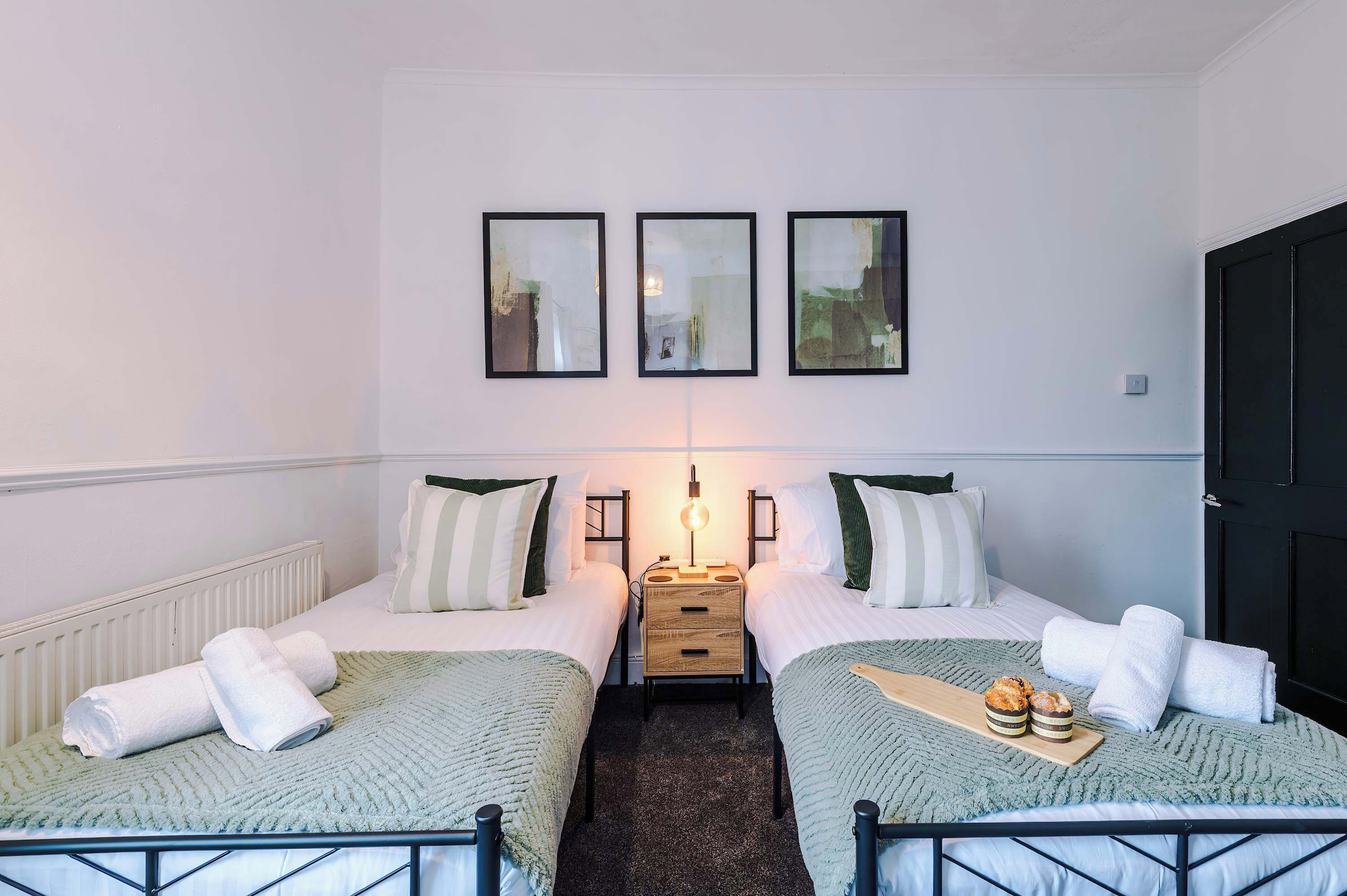 A double room with two beds, a nightstand, and a wall-mounted lamp.