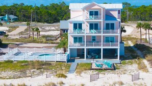 A multi-story beachfront property with a swimming pool, beach chairs, and a fenced patio area. - Siren's Song - Beach front, Private Pool, Island Luxury! (St. George Island)