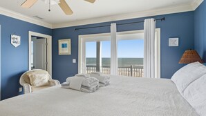 A bedroom with a large bed, a chair, a view of the ocean, and a ceiling fan. - Siren's Song - Beach front, Private Pool, Island Luxury! (St. George Island)