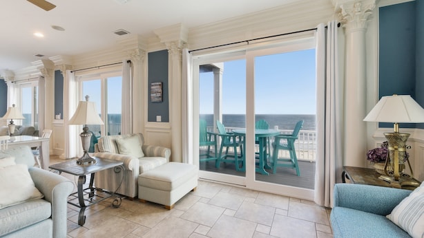 A spacious living room with a view of the ocean, a balcony with chairs, and a dining area. - Siren's Song - Beach front, Private Pool, Island Luxury! (St. George Island)