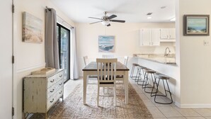 Un espace repas comprenant une table et des chaises, un ventilateur de plafond et des œuvres d’art accrochées aux murs.