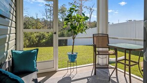 A covered patio with a table and chairs, a potted plant, and a view of a grassy yard and trees. - NEW Coastal Retreat • Fire Pit • Golf Escape • 3 mi to Holden Beach • Sleeps 6 (Supply)