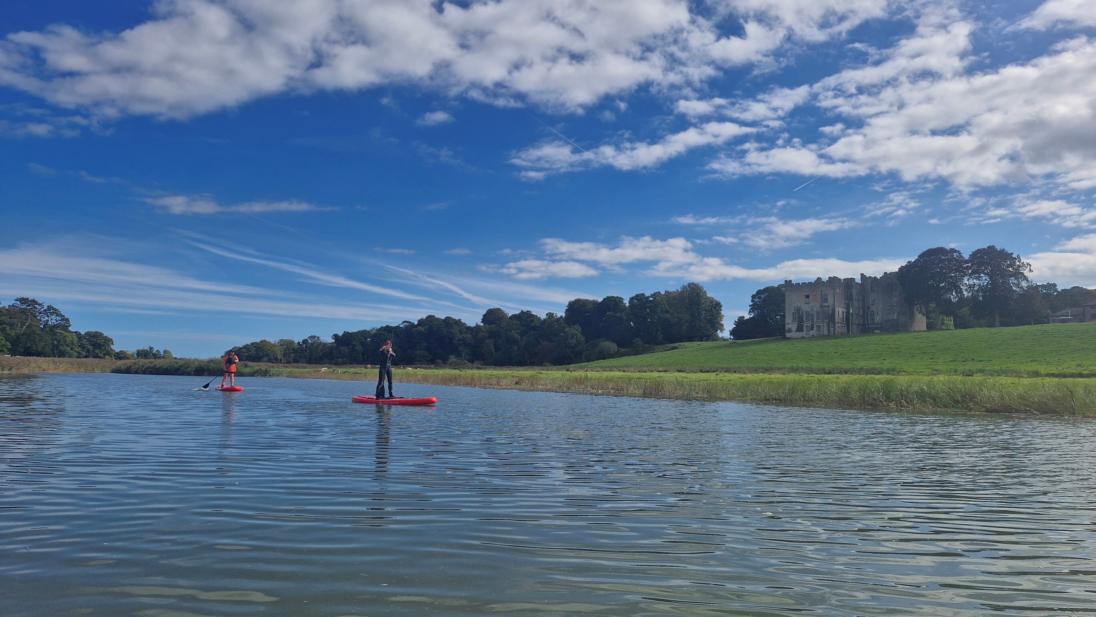 Een rustig meer met paddleboards, een kasteel op de achtergrond en een heldere lucht.