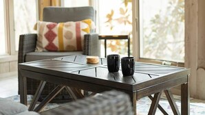 Une pièce chaleureuse avec une table dressée pour deux personnes, une chaise dotée d’un coussin à motifs et une fenêtre donnant sur des arbres.
