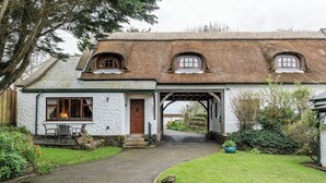 Een traditioneel huis met rieten dak, een stenen boogvormige entree en een kleine tuin met een pad naar de voordeur.