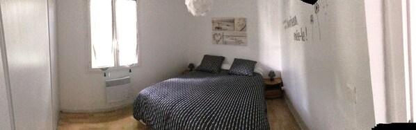 Une petite pièce étroite, avec un lit, un radiateur et une fenêtre.