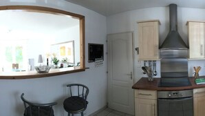 A compact kitchen with a built-in oven, a coffee machine, and a sink. There is a chair and a small dining table. - Contemporary, single-storey house (Corme-Royal)