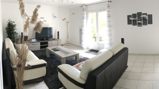 A modern living room with a sofa, coffee table, TV, and decorative plants. - Contemporary, single-storey house (Corme-Royal)