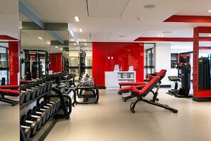 Une salle de sport équipée de matériel de musculation, de miroirs et agrémentée de touches de couleur rouge.
