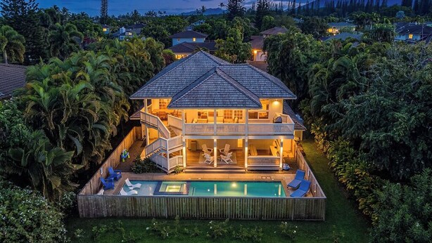 Una casa de dos pisos con piscina, rodeada de exuberante vegetación.