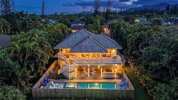 Une maison à deux étages avec une piscine, entourée d’une végétation luxuriante.