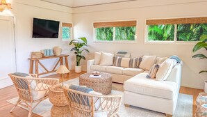 Un salón con sofá, sillas, mesa de centro, televisor y ventanas con vistas a zonas verdes.