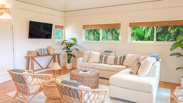 A living room with a sofa, chairs, a coffee table, a TV, and windows with a view of greenery.