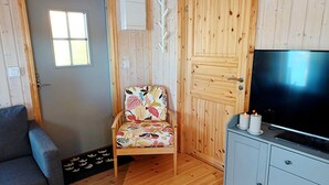 Une pièce chaleureuse avec un plancher en bois, un canapé gris, un fauteuil à motifs floraux, une télévision et un meuble.