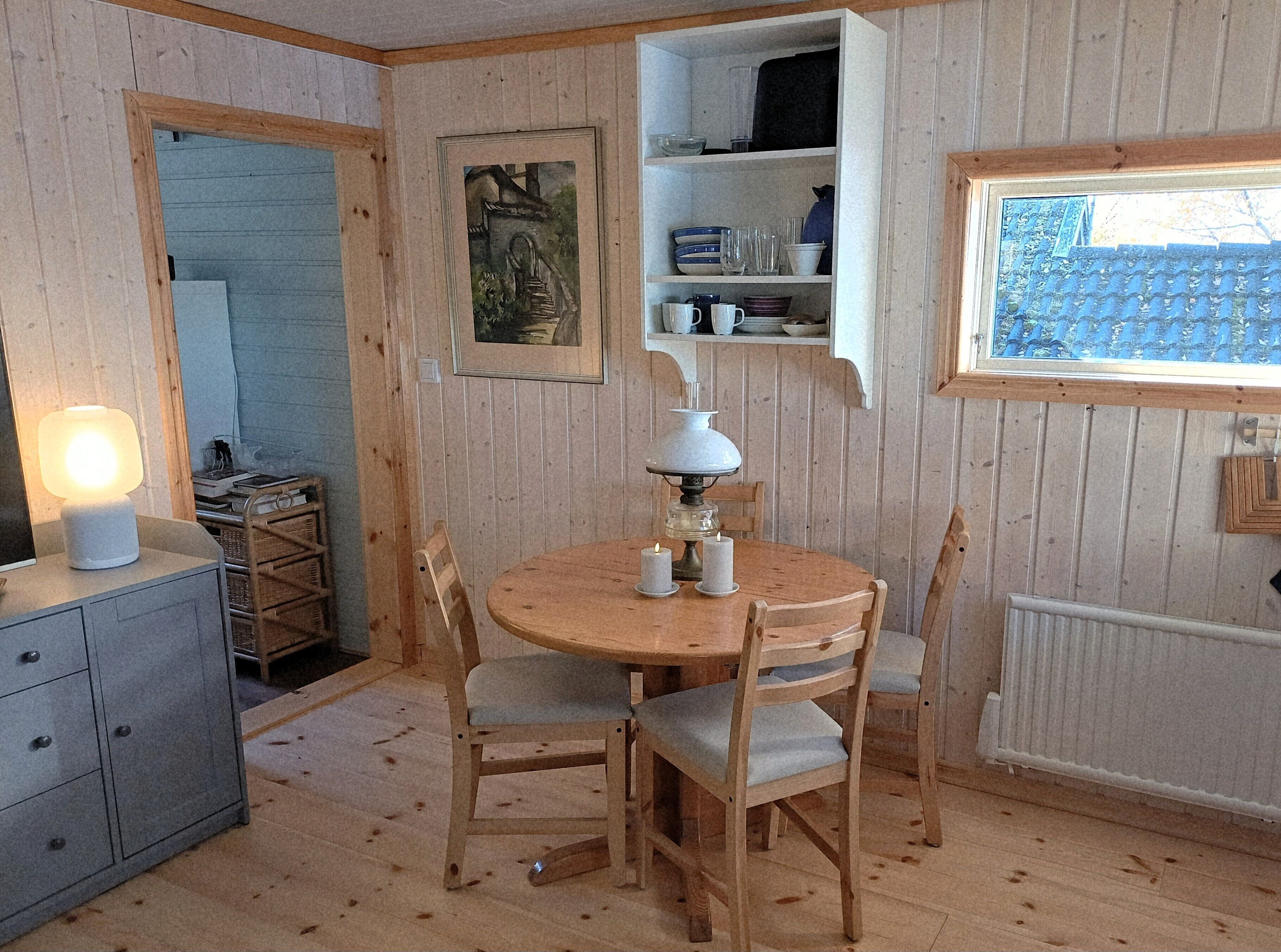 A cozy room with a wooden dining table, chairs, a lamp, and a shelf with dishes.