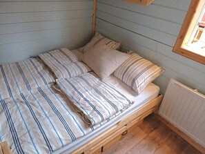 A small, single-bed room with striped bedding, wooden headboard, and a window with a view of the outside.