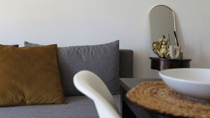 A modern living room with a grey sofa, a brown cushion, a white chair, a round table with a bowl, and a decorative item on a side table.
