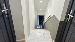 A narrow hallway with a marble floor leading to a staircase.