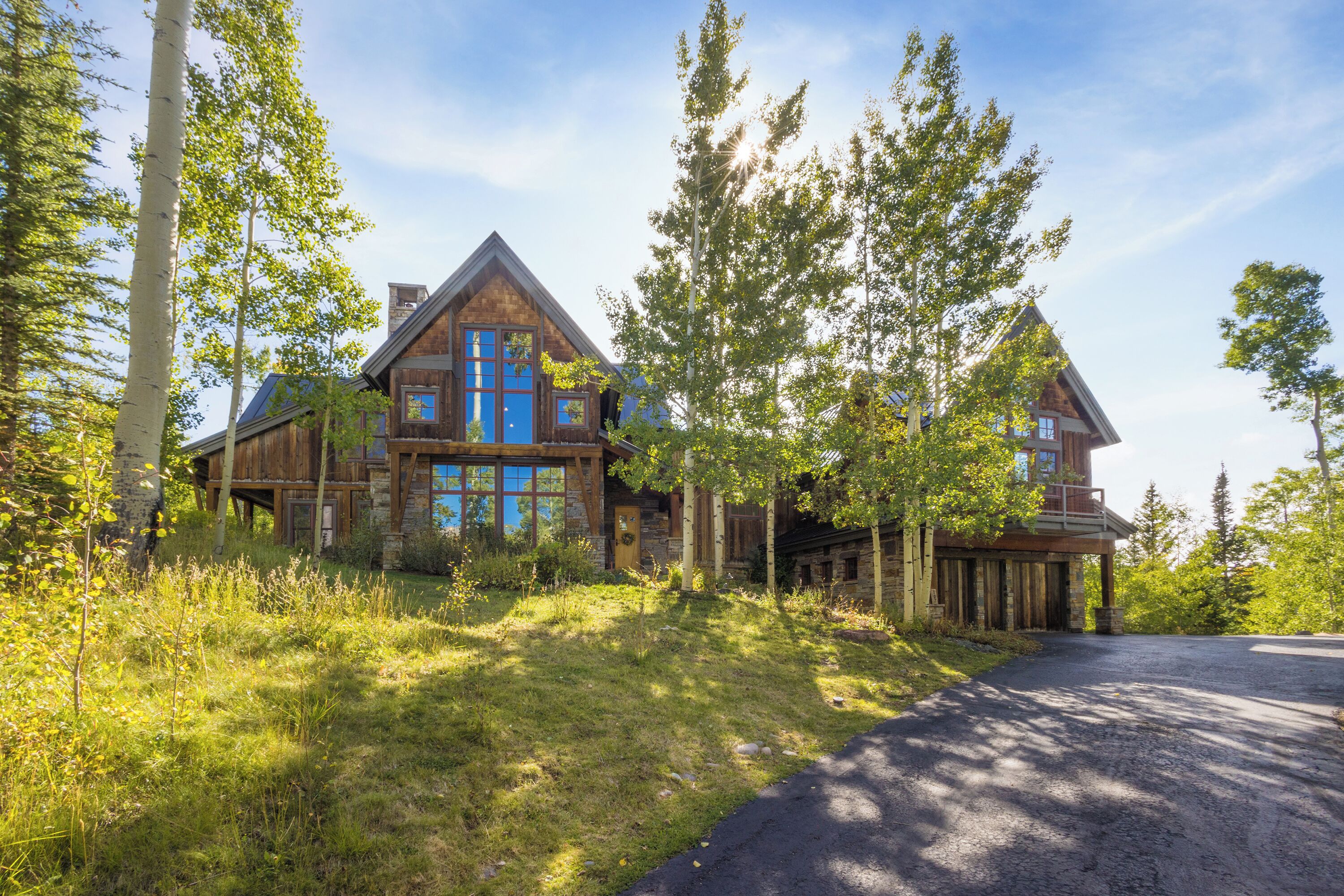 A large log cabin with a prominent blue door and multiple windows, surrounded by tall trees and a grassy area.