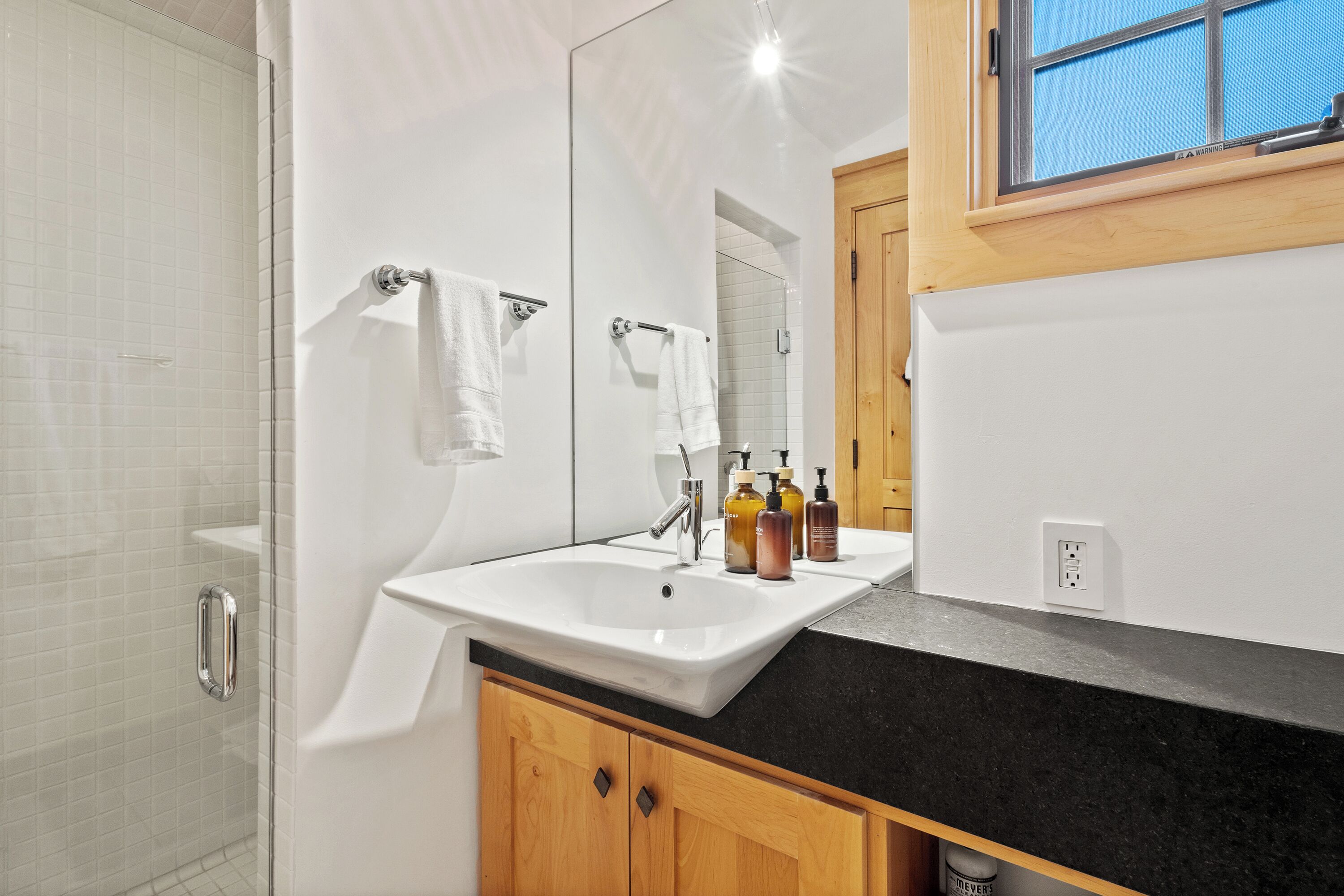 Une salle de bain avec un lavabo blanc, des meubles en bois, un miroir et un espace douche.