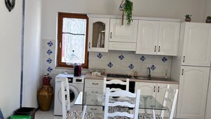 A compact, well-lit room with a bed, a dining table with chairs, a washing machine, and a sink. - Sailor's House (Milazzo)