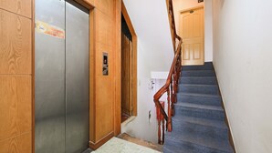 Een houten lift met een rookverbodssymbool, een digitaal scherm en een betegelde trap met een houten leuning.