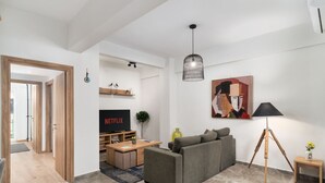 A modern living room with a grey sofa, a wooden coffee table, a TV displaying 'NETFLIX', a floor lamp, and a painting on the wall. - Acropolis Oasis - 2BR, Koukaki (Athina)