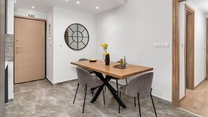 A modern dining area with a wooden table and four chairs, a vase with flowers, and a wall-mounted clock. - Acropolis Oasis - 2BR, Koukaki (Athina)