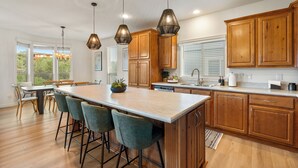 A modern kitchen with wooden cabinets, a large island with bar stools, pendant lighting, and a view of the outdoors.
