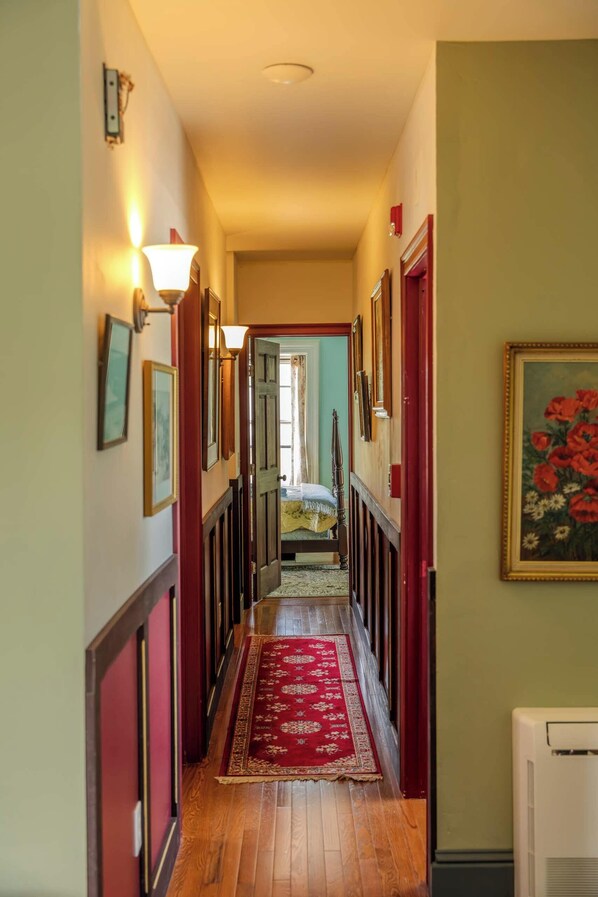 Un pasillo con piso de madera, alfombra roja y una cama al final.