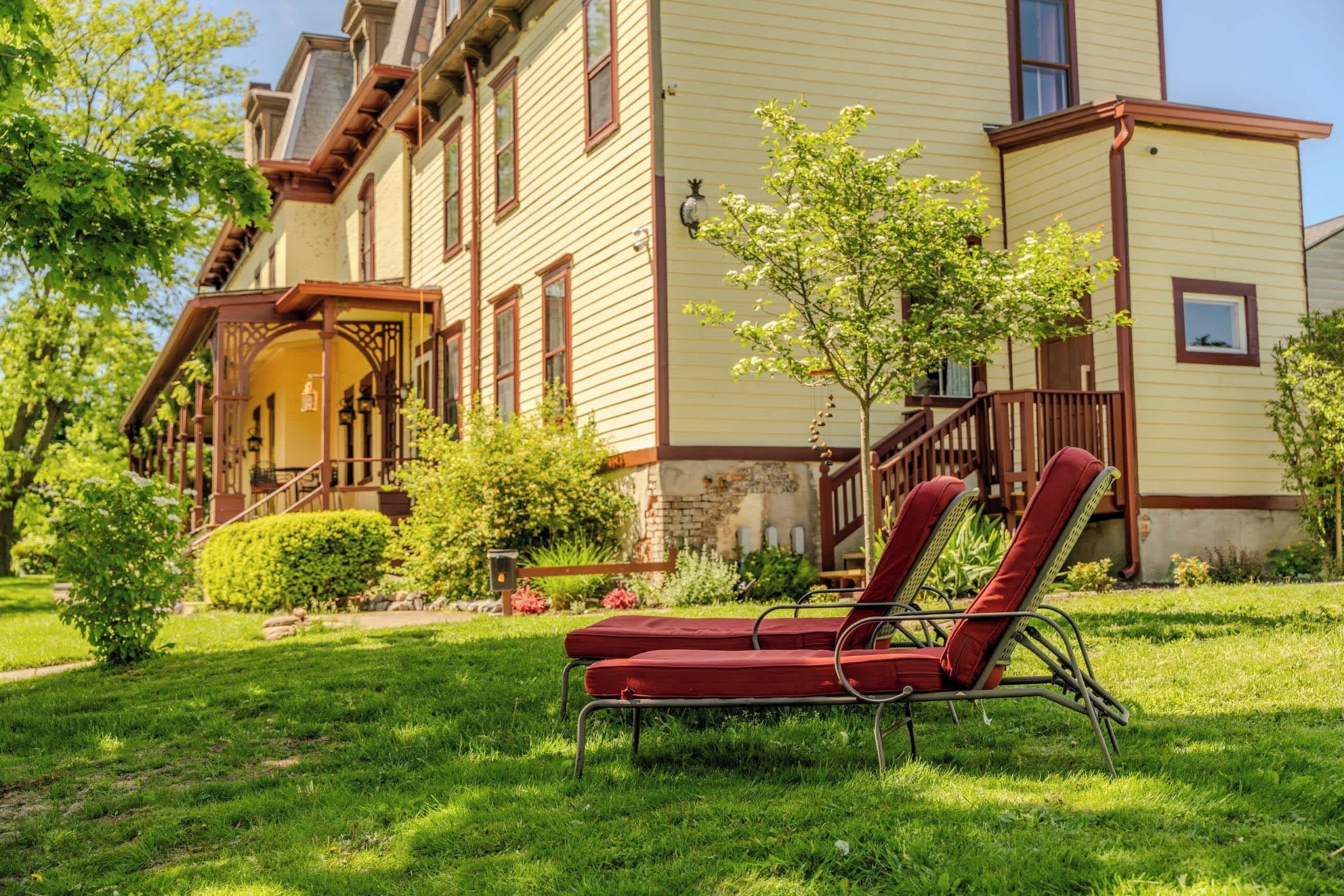 A two-story house with a front porch, a small garden, and a red lawn chair.