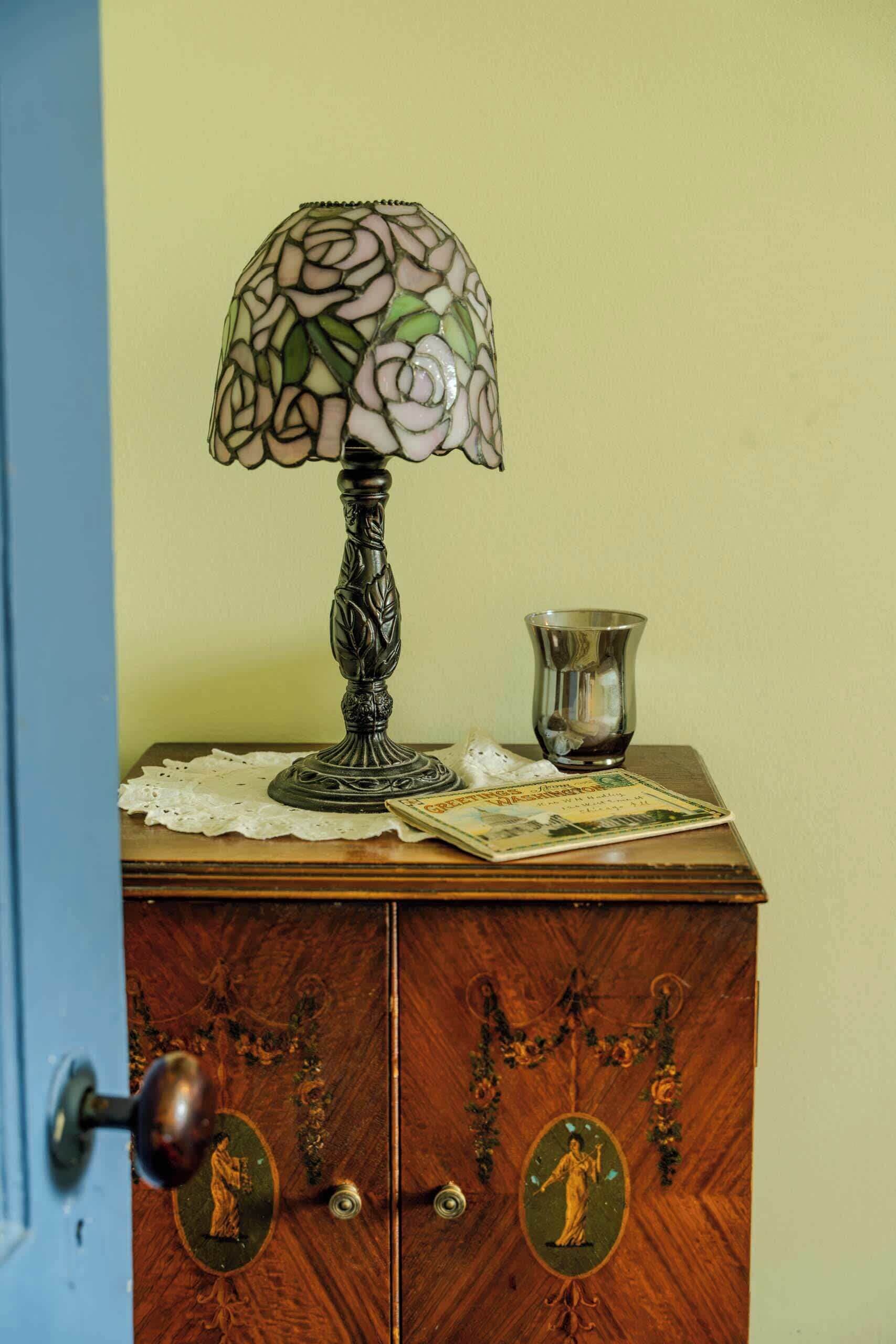 Un mueble de madera con una jarrón de vidrio y una lámpara de vitral encima.