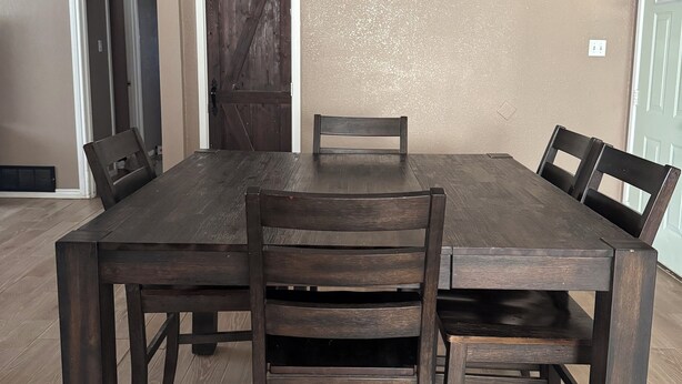 A dining room with a large wooden table, four chairs, a ceiling fan, and a door in the background. - 3-bedroom house near Texas Tech University (Lubbock)