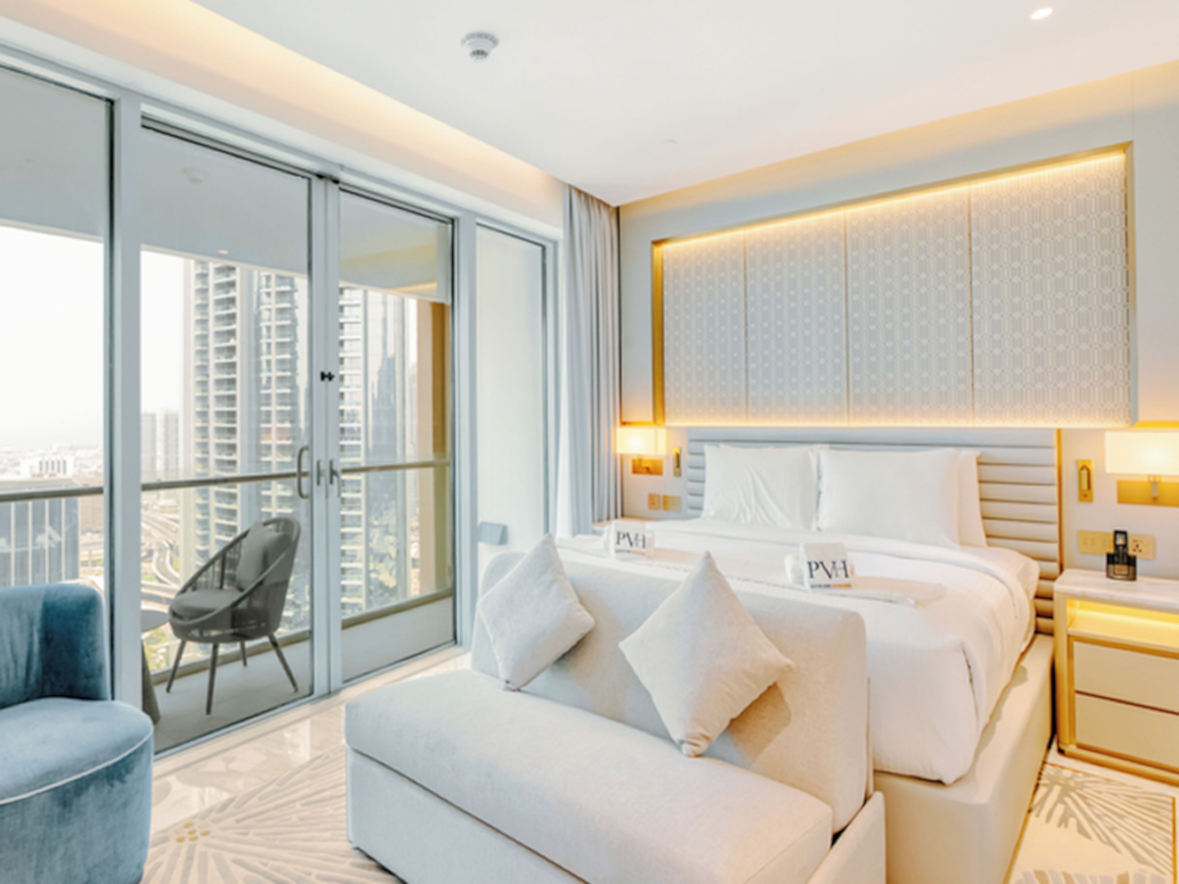 Une chambre d’hôtel moderne dotée d’un grand lit, d’un canapé, d’un fauteuil et d’un balcon offrant une vue sur la ville.