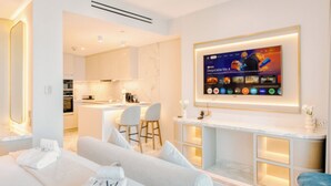 Een moderne hotelkamer met een bank, een tv die aan de muur is bevestigd en een keuken in de achtergrond.