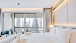 Une chambre d’hôtel moderne dotée d’un grand lit, d’un coin salon avec un fauteuil et offrant une vue sur la ville grâce à de grandes fenêtres.