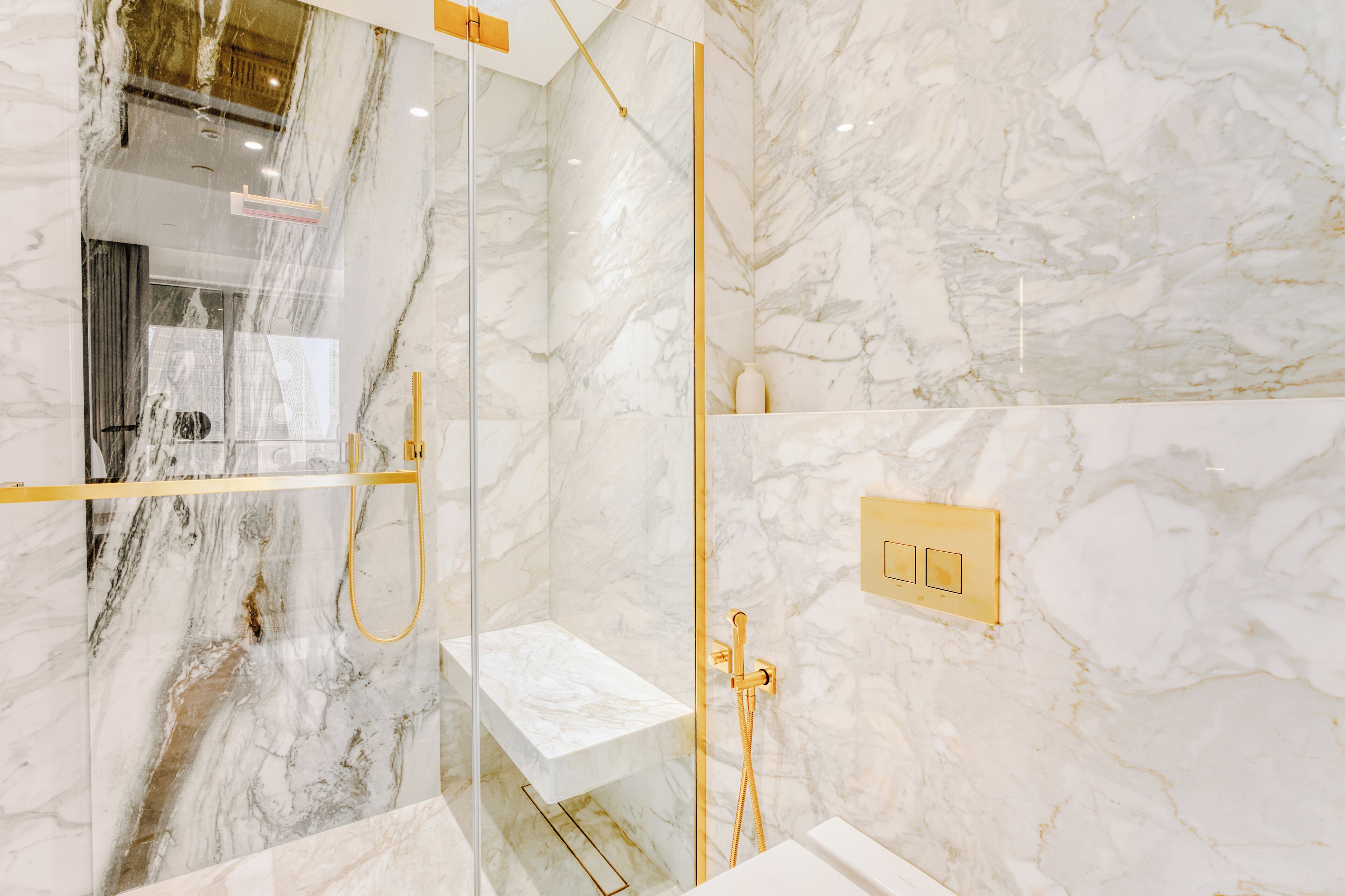A modern bathroom with marble walls, a glass-enclosed shower, and gold fixtures.