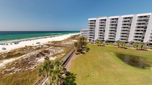 Un hotel frente a la playa con varios balcones, una playa de arena y un césped.