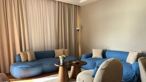 Ein modernes Wohnzimmer mit einem blauen Modulsessel, einem beigen Sessel und einem runden Couchtisch aus Holz.