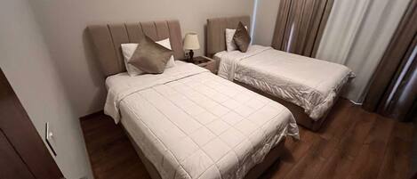 A hotel room with two beds, a wooden floor, and a window with curtains.